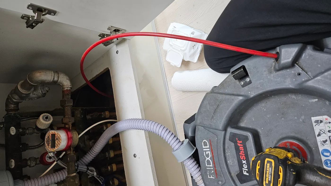 싱크대 하부장 앞에 놓인 RIDGID 플렉스샤프트 장비와 바닥 배관으로 들어가는 빨간 샤프트